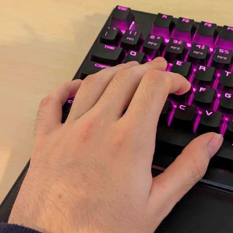 Main posée sur un clavier mécanique de PC rétroéclairé, doigts sur les touches de la rangée supérieure