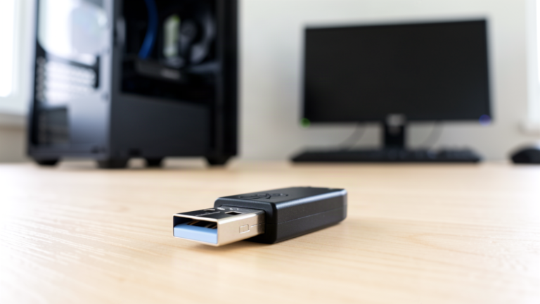 Clé USB noire posée sur un bureau en bois devant un PC de bureau Windows