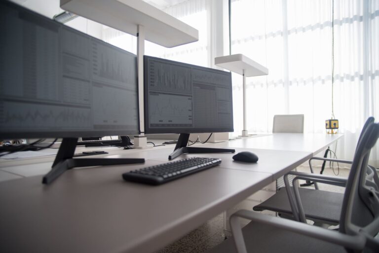 Deux écrans de PC, un clavier noir et une souris sur un bureau clair