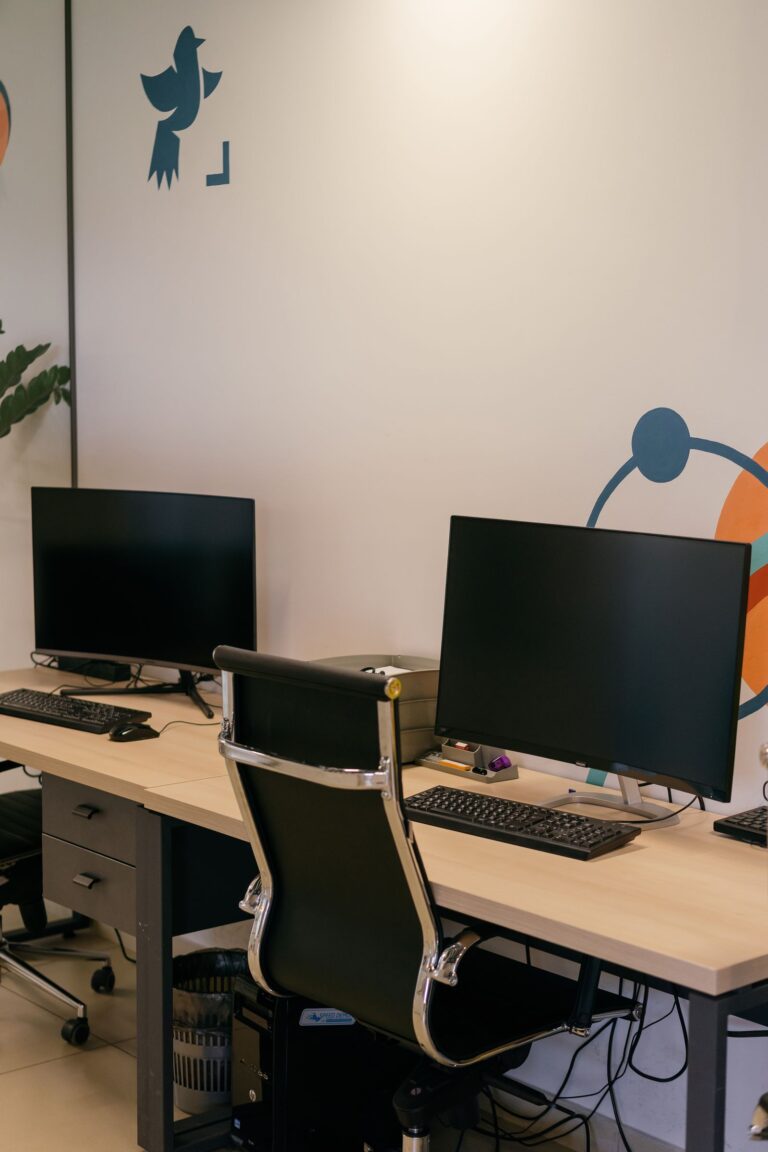 Deux postes de travail avec écrans, claviers noirs et unités centrales de PC sous le bureau